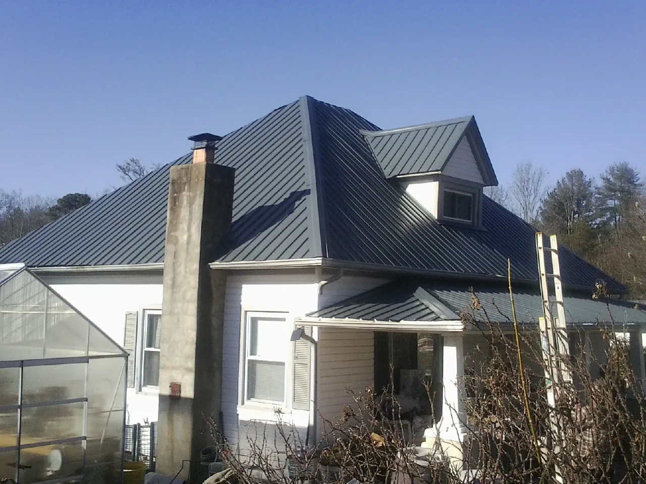 Dark blue standing seam metal roof on a white farmhouse with dormer — Slate & Tile Roof Repair by Roofing Brothers in Hortense
