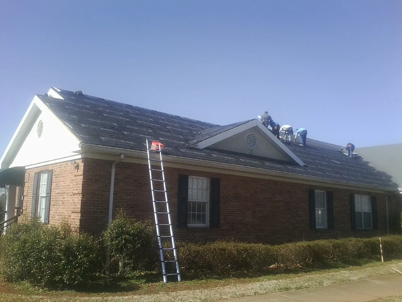 Crew tearing shingles off a brick ranch roof with a ladder set — Emergency Roof Repair work by our crew in Hortense