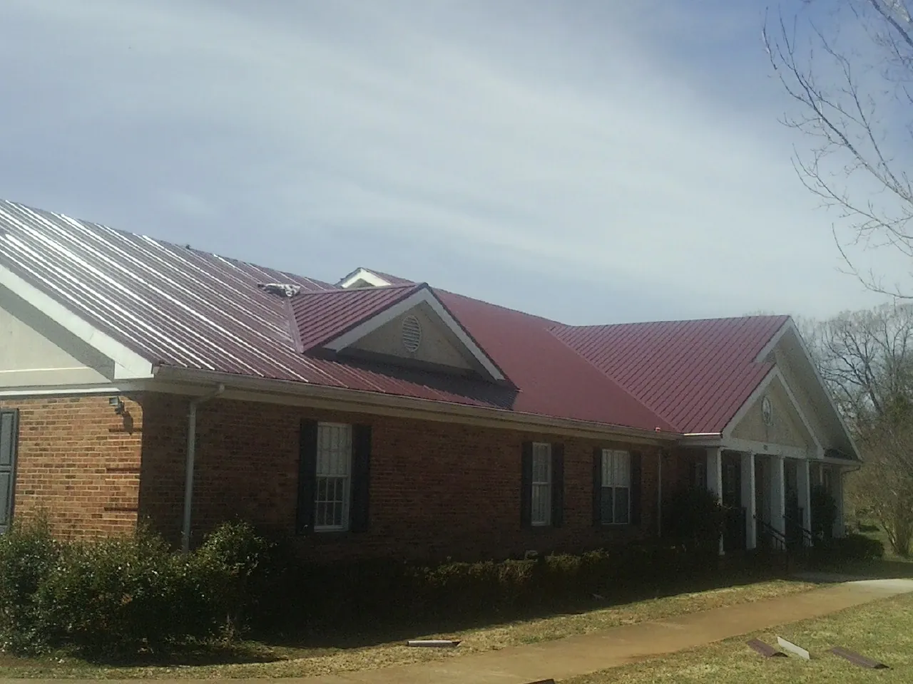 Red metal roof with gabled entries on a long brick building, from a Hail Damage Roof Repair job in Hortense