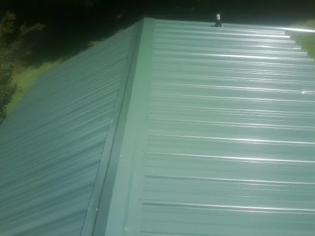 New green metal panels meeting at the ridge of a roof — Flat Roof Repair work by our crew in Hortense