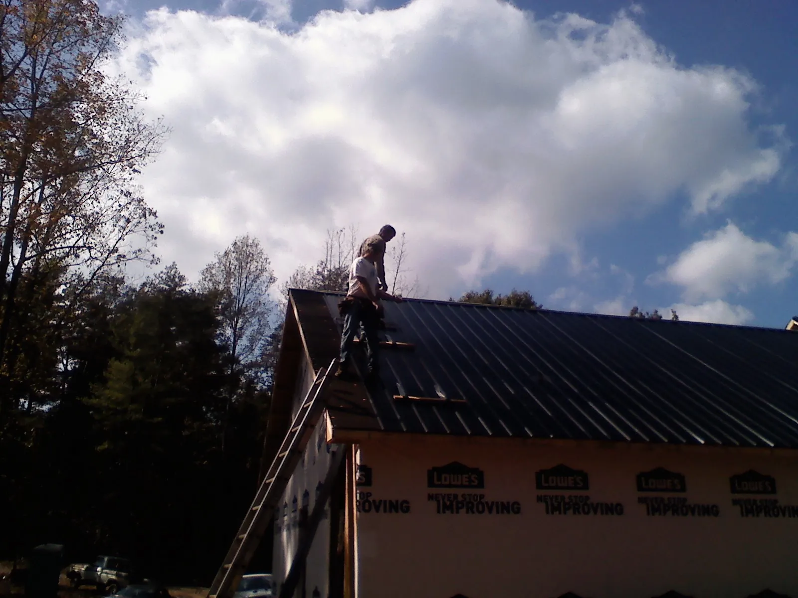 Roofer fastening dark metal panels high against a cloudy sky, from a Roof Inspection job in Hortense