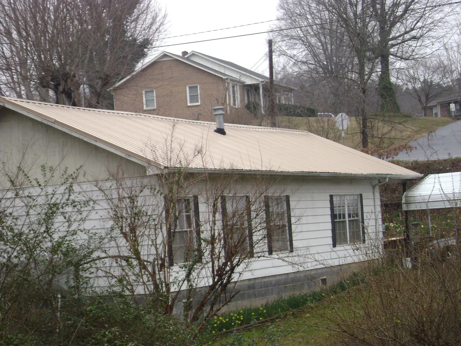 Tan metal roof on a white sided house set into a hillside — Commercial Roofing by Roofing Brothers in Hortense